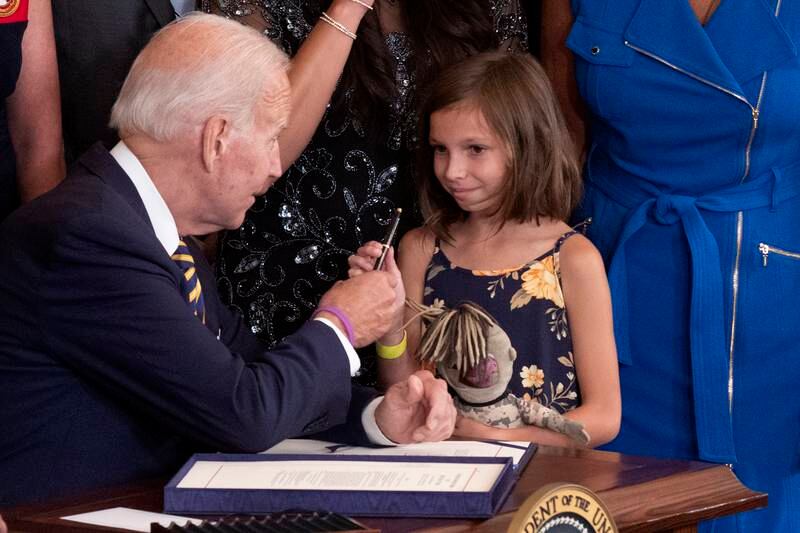 Mr Biden hands the pen used to sign the act into law to Brielle Robinson, the surviving daughter of Sergeant First Class Heath Robinson. EPA