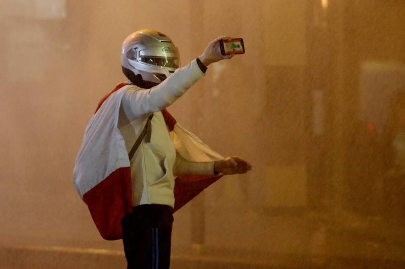 An anti-government protester is sprayed by a water cannon as he films by his mobile phone during a protest against the new government, near the parliament square, in Beirut. AP Photo