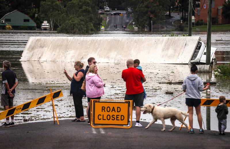 People stand on a flooded road as they look at a truck that was pushed onto its side by floodwaters. Getty Images