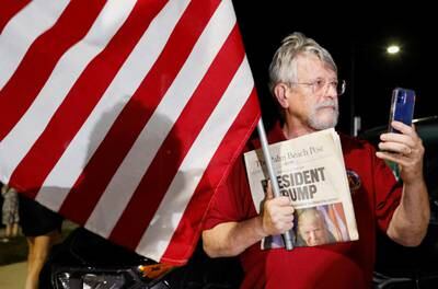 A supporter of Mr Trump holds a flag and an old newspaper outside the former president's Mar-a-Lago home. Reuters