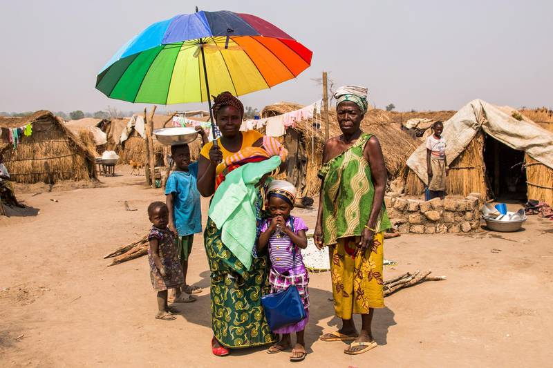 A family shelter from the midday sun beneath a parasol in a sprawling camp for thousands of families displaced by civil war in Kaga Bandoro, the Central African Republic
