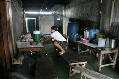 A woman gets water from a container as she steps on an improvised foot bridge inside her house.