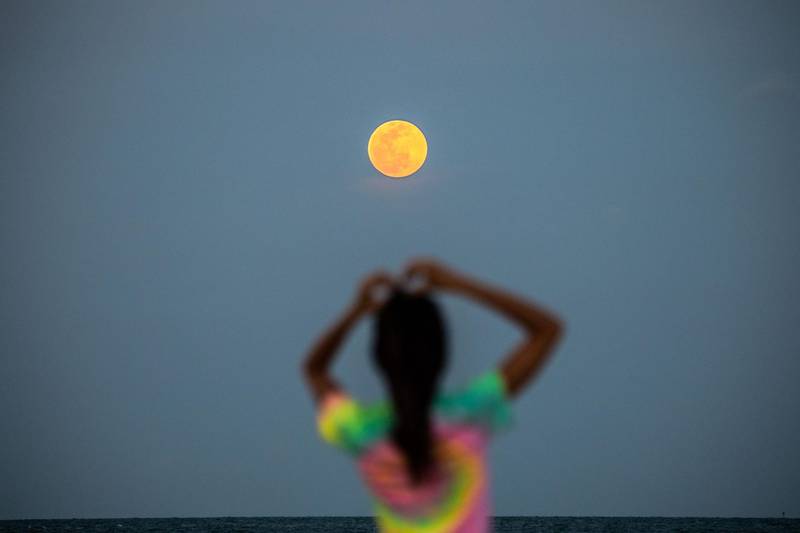 A pink supermoon is seen in the background as people relax on the beach in Miami Beach, US, on June 24, 2021. Four supermoons will grace the skies in 2022. AFP