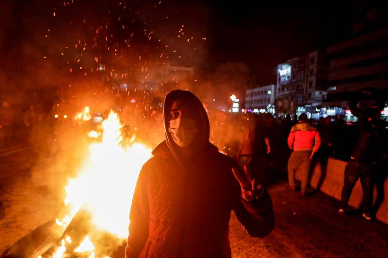 An anti-government protester flashes the victory gesture while tyres are set aflame as demonstrators cut off a section of the Beirut-Byblos highway in Byblos, as they protest the newly-announced government formed by Prime Minister Hassan Diab.  AFP