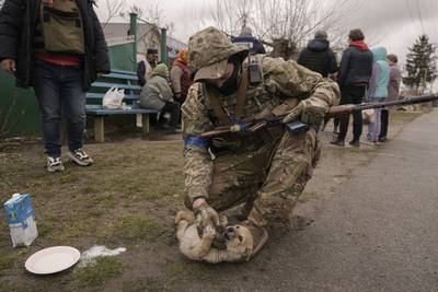 A Ukrainian soldier tries to convince a puppy to drink milk as residents wait for distribution of food products in Motyzhyn, Ukraine, which was until recently under the control of the Russian military. AP