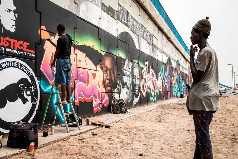 A man looks on as a member of Radikal Bomb Shot (RBS) collective, a collective of Senegalese artists, paints a mural depicting key American and African anti-racism activists, in a show of support for the Black Lives Matter movement in Dakar.  AFP