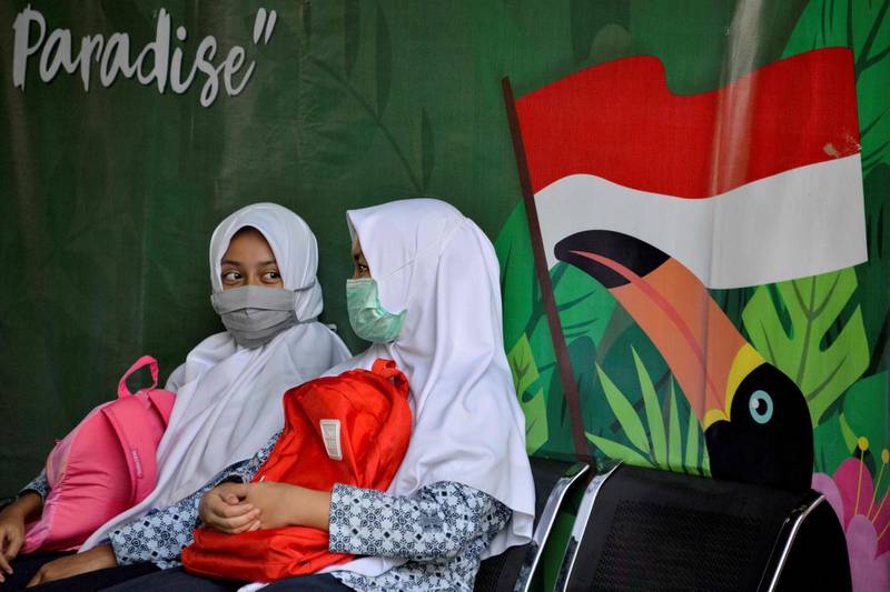 Students, wearing face masks amid the coronavirus pandemic, sit by a mural depicting the Indonesian flag at an Islamic junior high school in Banda Aceh.  AFP