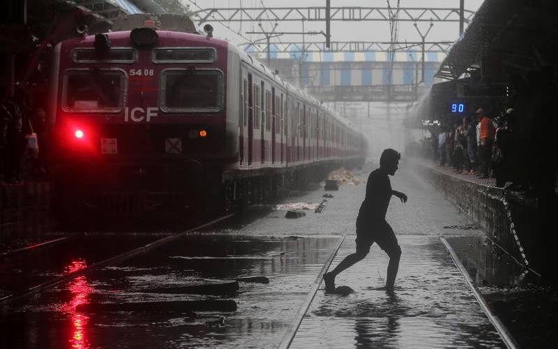 A commuter crosses waterlogged railway tracks as a suburban train is seen parked at a railway station after its services were suspended during heavy monsoon rains in Mumbai. Reuters