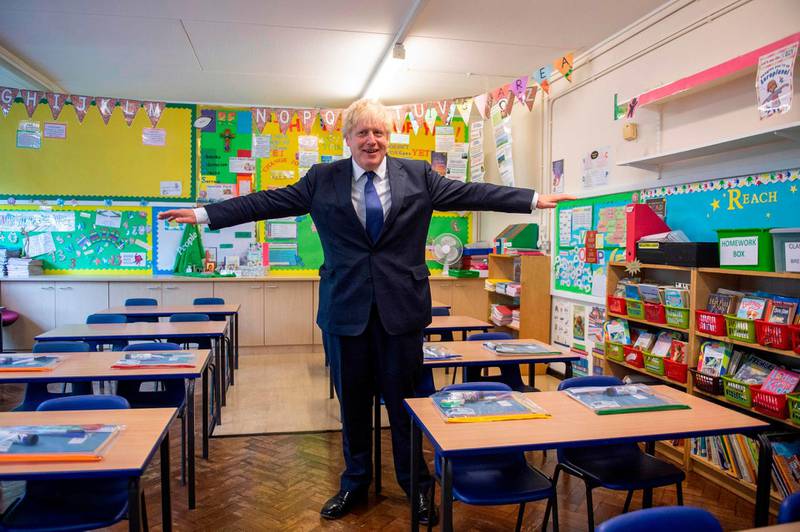 Britain's Prime Minister Boris Johnson poses with his arms out-stretched in a classroom as he visits St Joseph's Catholic Primary School in Upminster, east London, on August 10, 2020 to see preparedness plans implemented ahead of the start of the new school year as a response to the novel coronavirus pandemic.  / AFP / POOL / Lucy YOUNG
