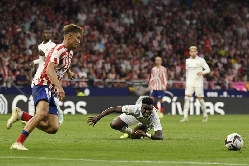 Atletico Madrid midfielder Marcos Llorente chases after the ball as Vinicius Junior lies on the turf. AFP