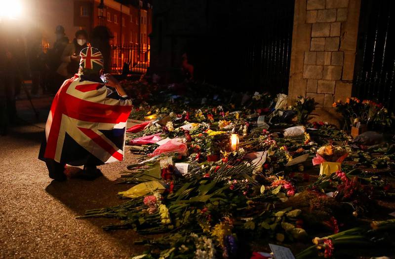 A mourner draped in a British Union Jack flag takes pictures of flowers placed outside Windsor Castle. Reuters