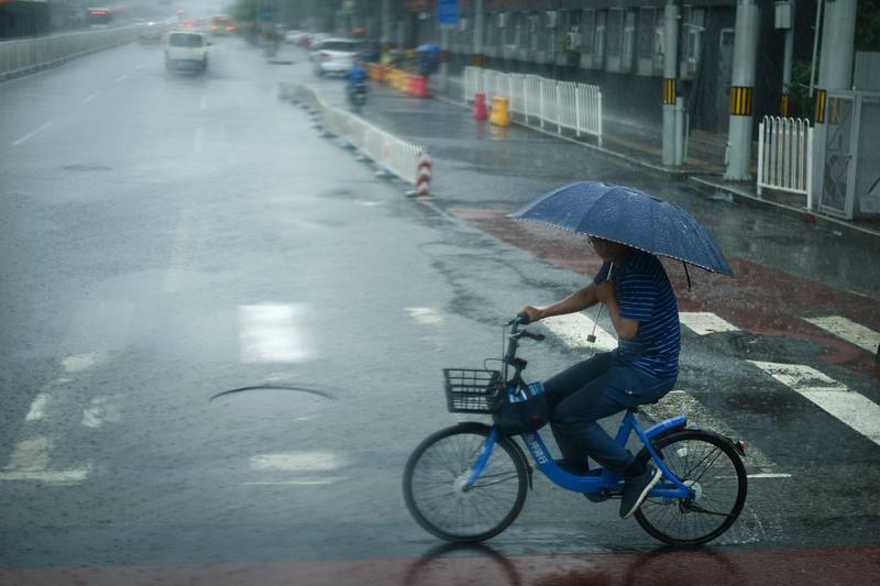 A man holds an umbrella as he rides a shared bicycle along a street on a rainy day in Beijing. Wang Zhao/AFP