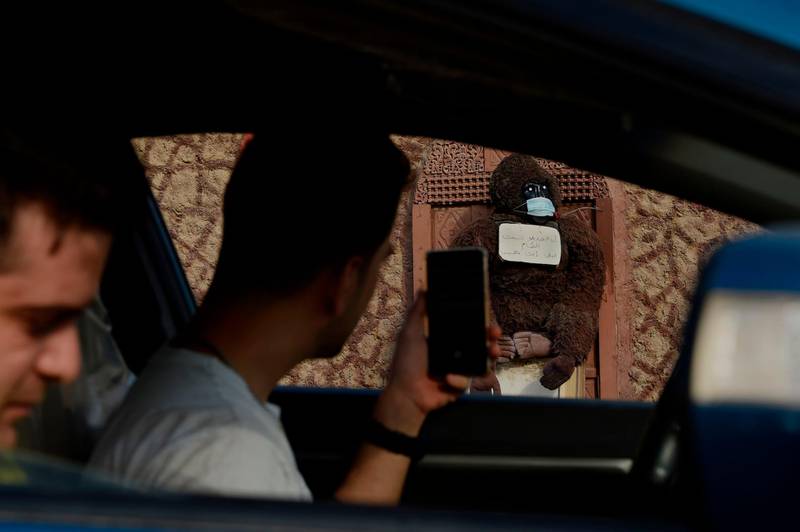 A motorist stops to take a picture with his cell phone of a stuffed gorilla wearing a face mask with a sign reading in Arabic "I, the gorilla, wore a mask, why don't you wear (one)?", placed by a homeowner outside to encourage people to wear protective gear, in Hamad Town, south of Bahrain's capital Manama.   AFP