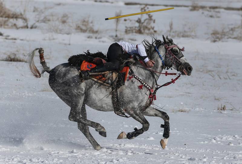 A player performs acrobatics while riding his horse at full gallop, to avoid being hit by a javelin during a game of jereed in Erzurum, Turkey. EPA