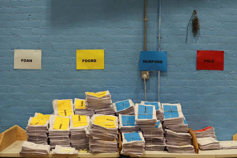 Colour-coded stacks of votes are pictured under posters with names of candidates for the Tiverton and Honiton by-election. Reuters