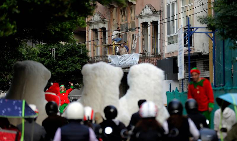 Workers restore the windows of a house as Lebanese youths dressed as Santa Clause, polar bears and Santa's helpers parade ahead of Christmas along Gouraud street in the capital Beirut's Gemmayzeh neighbourhood, one of the hardest hit by a massive explosion that shook the city on August 4, causing extensive damage to buildings and leaving scores of people dead or injured.  AFP