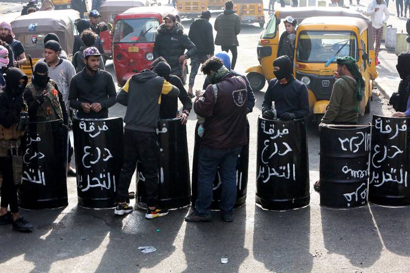 Iraqi anti-government protesters carry black shields made out of metal drums, on which they had painted the words "Tahrir Shield Squad.", as they gather at al-Sinek bridge in the capital Baghdad. AFP