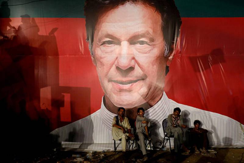 FILE PHOTO: Labourers, who set up the venue, sit under a wall with a billboard displaying a photo of Imran Khan, chairman of the Pakistan Tehreek-e-Insaf (PTI), political party, as they listen to him during a campaign rally ahead of general elections in Karachi, Pakistan July 22, 2018. REUTERS/Akhtar Soomro/File Photo