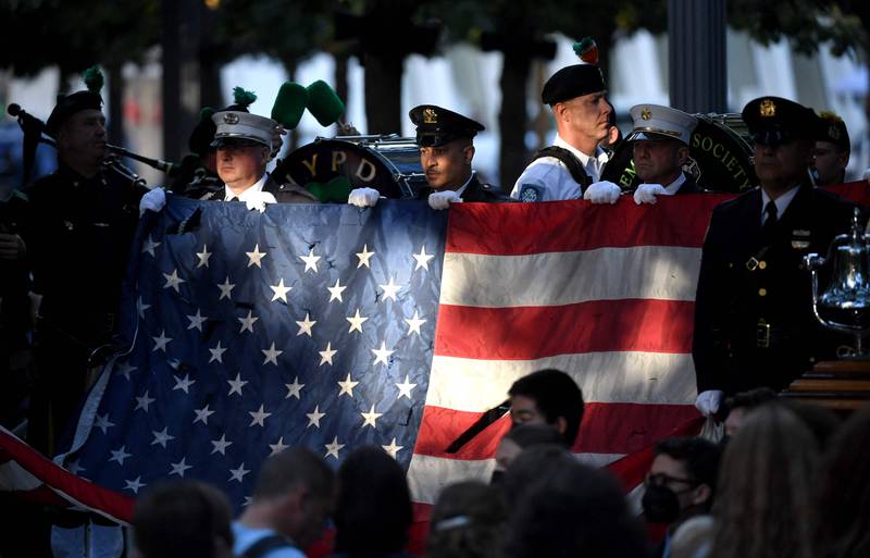 New York police and firefighters hold a US flag as a band plays the US National Anthem at the National 9/11 Memorial during a ceremony commemorating  the 20th anniversary of the 9/11 attacks on the World Trade Center, in New York.  AFP