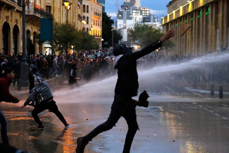 Anti-government protesters throw stones at the riot police during ongoing protests in Beirut, Lebanon, Wednesday, Jan. 22, 2020.  Lebanon's new government has held its first meeting a day after it was formed following a three-month political vacuum. (AP Photo/Bilal Hussein)