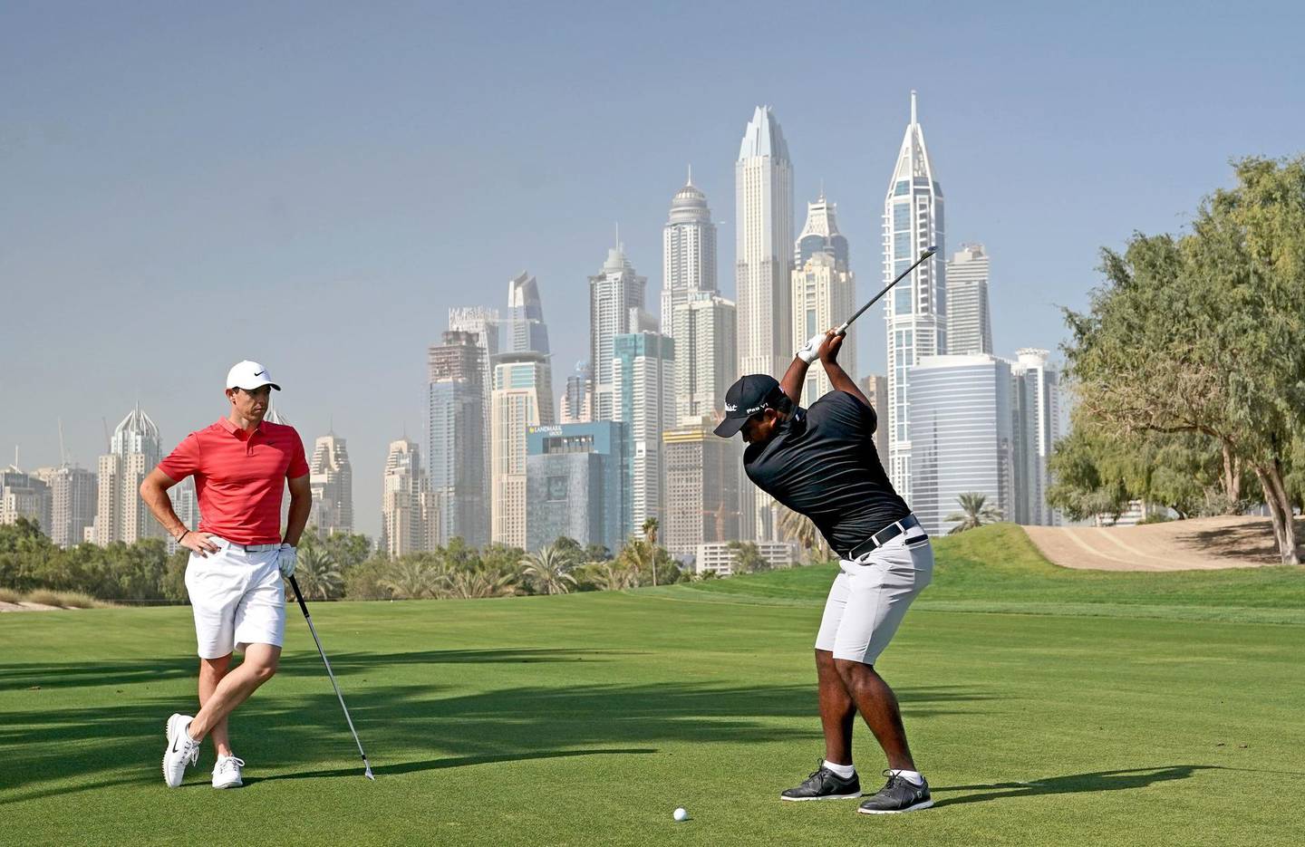DUBAI, UNITED ARAB EMIRATES - JANUARY 23: Rayhan Thomas of India plays his second shot on the par 5, 13th hole watched by Rory McIlroy of Northern Ireland as a preview for the Omega Dubai Desert Classic on the Majlis Course at The Emirates Golf Club on January 23, 2018 in Dubai, United Arab Emirates.  (Photo by David Cannon/Getty Images)