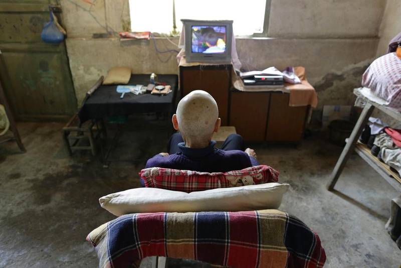 Qin Wenji, 82, who suffers from skin cancer, watches TV in his bedroom at Heshan village. Jason Lee / Reuters