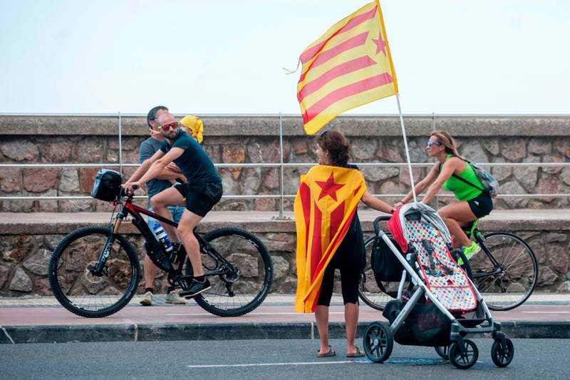 A man on his bike looks at a woman with Catalonian pro-independence flags on August 12, 2017 in the northen Spanish Basque city of Donostia (San Sebastian) during a demonstration in support of Catalonia and its planned referendum on independence from Madrid to be held on October 1.
The demonstration was symbolic, in a region still marked by decades of violence waged by armed separatist group ETA, and where the desire for independence remains strong despite the current peaceful times. / AFP PHOTO / GARI GARAIALDE