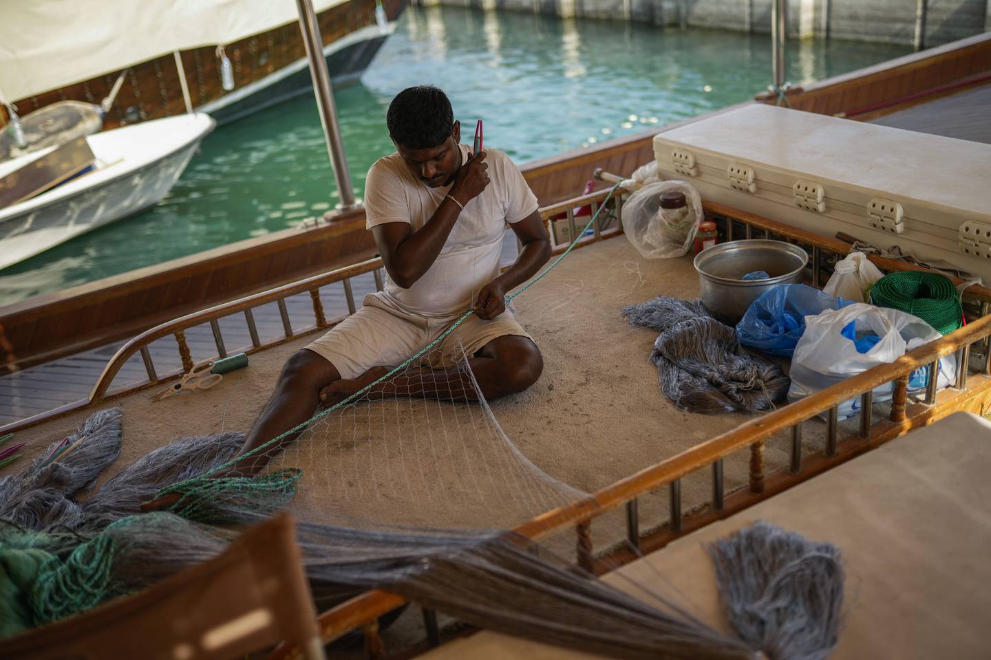 A man on a wooden boat at harbour in Doha bay sews a fishing net to be sold in Souq Waqif market. AP Photo