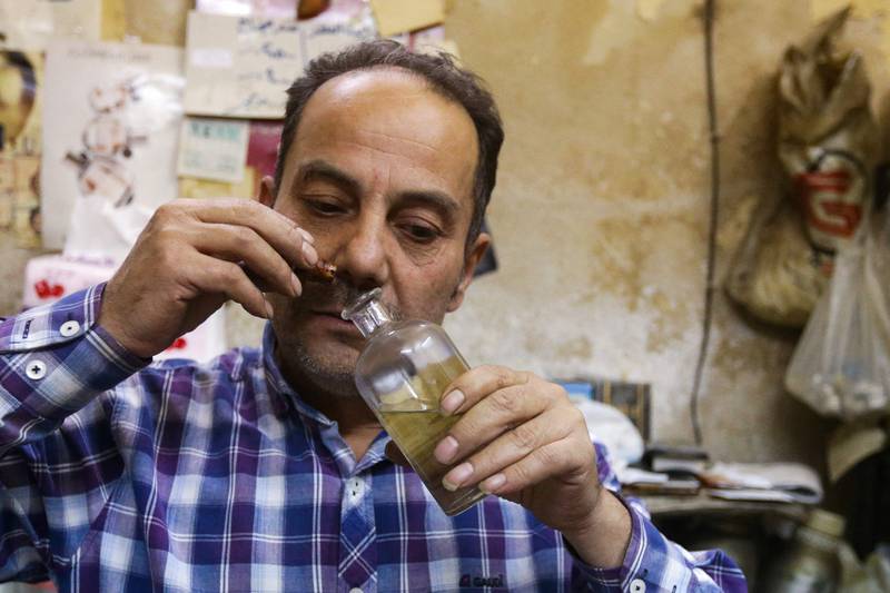 Syrian perfumer Mohammad al-Masri works at his shop in a historic souq of Damascus's old city on October 31, 2022.  - One whiff of a fragrance is all al-Masri needs to recreate the scents of luxury brands, for a fraction of the cost.  Dozens of customers flock daily to his tiny store in Damascus's old city, many flashing photos on their phones of high-end perfumes they want to replicate.  "All I have is my shop, and this nose I've been training since I was 15," the 55-year-old told AFP, pointing at his nose.  (Photo by LOUAI BESHARA  /  AFP)