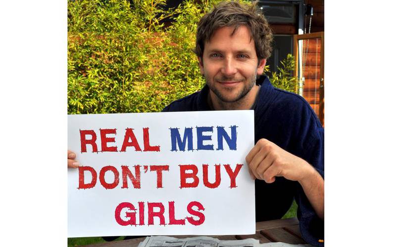 Bradley Cooper holds up a sign reading Real Men Don’t Buy Girls. Courtesy Bradley Cooper