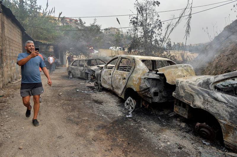 A man takes a picture of a row of burnt-out cars.  EPA