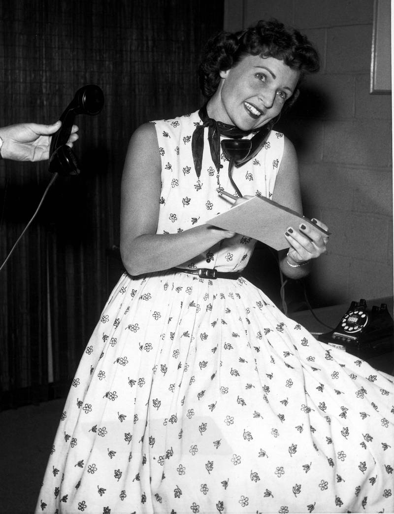 Betty White, in a black and white floral dress, poses on the phone in a Hollywood studio in 1957. Press Wire
