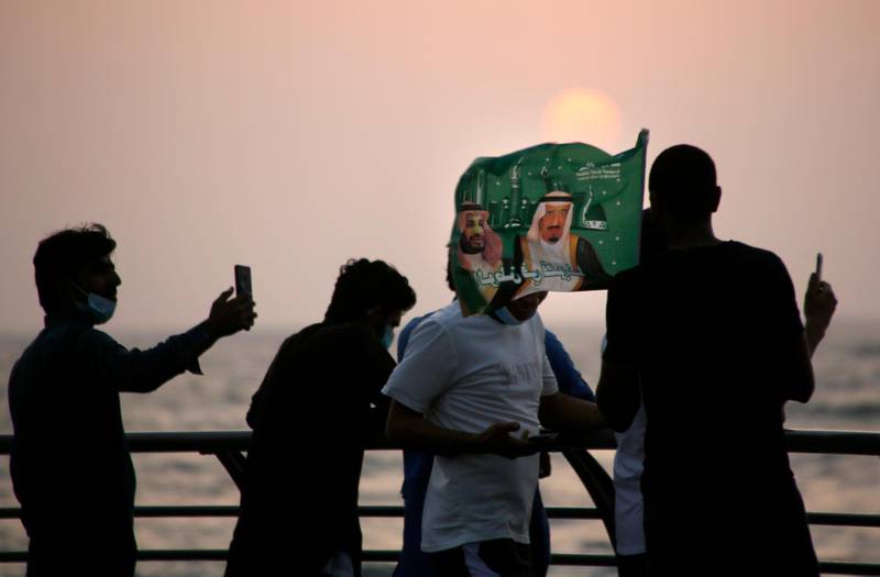 Saudis watch the sunset as they wave a flag with pictures of Saudi King Salman and Crown Prince Mohammed bin Salman, marking National Day to commemorate the unification of the country as the Kingdom of Saudi Arabia, in Jeddah. AP Photo