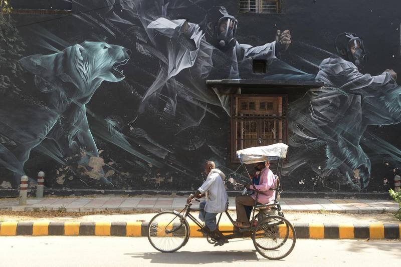 A rickshaw driver carries passengers wearing facemasks past a mural at Lodhi Art District during a government-imposed nationwide lockdown, in New Delhi, India.  AFP