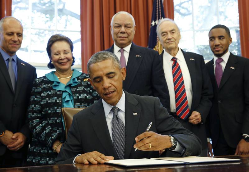 Powell and his wife Alma stand over Barack Obama as the then-president signs America's Promise Summit Declaration at the White House in September 2014. Reuters