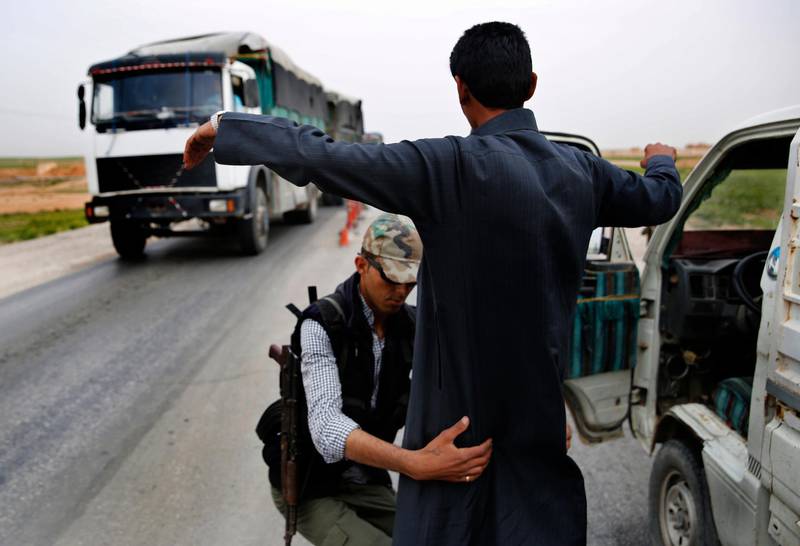 In this March 28, 2018 photo, a Kurdish policeman checks an Arab Syrian man at a checkpoint controlled by The U.S.-backed Syrian Democratic Forces, SDF, on a highway in Hassakeh province, Syria. SDF defeated IS in March but the Kurdish-led force is now facing protests by local Arab tribesmen in Deir el-Zour province. If the protests turn to an all-out uprising against the SDF it could be a blow to Washington as President Trump has plans to reduce America's military presence in Syria. (AP Photo/Hussein Malla)