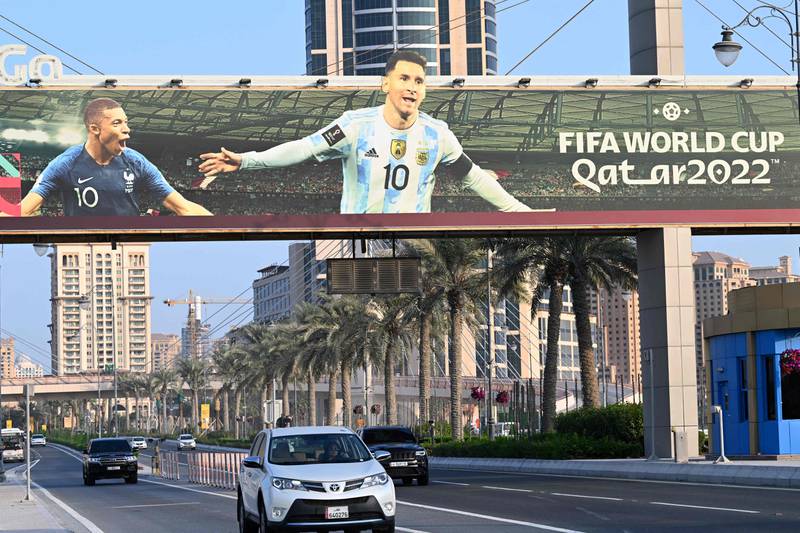Motorists drive past a billboard with pictures of France's striker Kylian Mbappe (L) and Argentine's captain Lionel Messi in Doha. AFP