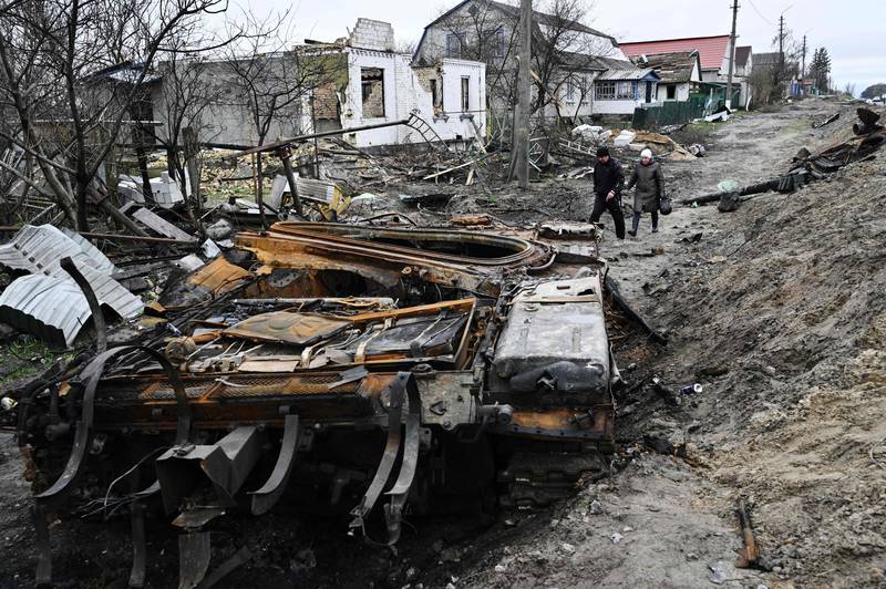 Residents walk amid debris of a charred Russian tank next to destroyed houses in the village of Zalissya. AFP