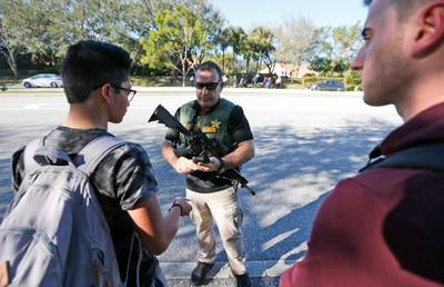 A law enforcement officer talks with students, Wednesday, Feb. 14, 2018, in Parkland, Fla. A shooting at Marjory Stoneman Douglas High School sent students rushing into the streets as SWAT team members swarmed in and locked down the building. Police were warning that the shooter was still at large even as ambulances converged on the scene and emergency workers appeared to be treating those possibly wounded. (AP Photo/Wilfredo Lee)