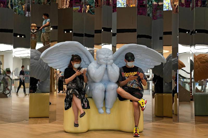A coronavirus masked couple sit on an angel statue browsing their smartphones at a shopping mall in Beijing, China. AP Photo