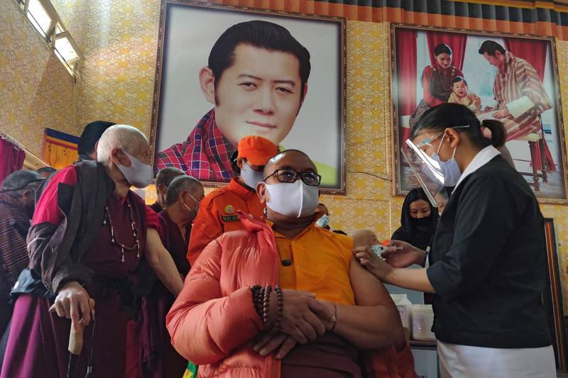 A health worker inoculates a dose of a COVID-19 coronavirus vaccine to a Buddhist monk sitting in front of a portrait of Bhutan's King Jigme Khesar Namgyel Wangchuck (top C) during the first day of vaccination in Bhutan, at Lungtenzampa Middle Secondary school in Thimphu on March 27, 2021.             / AFP / Upasana DAHAL
