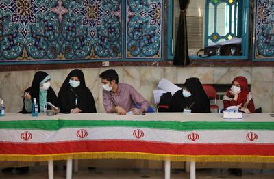 Electoral workers sit behind their desks decorated with the Iranian flag at a polling station during the presidential elections in Tehran, Iran. AP Photo