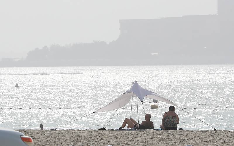 Beachgoers view a hazy skyline at Palm Jumeirah in Dubai. The conditions appear to be the tail of a storm that covered Iraq. Pawan Singh / The National