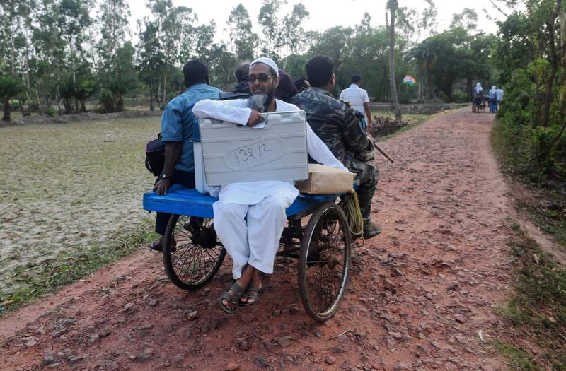 Indian election officials carry Electronic Voting Machine (EVM) and others materials on a tricycle to head to the polling station in Ghoramara island, about 110 km south of  Kolkata on May 18, 2019, ahead of the 7th and final phase of India's general election. / AFP / DIBYANGSHU SARKAR
