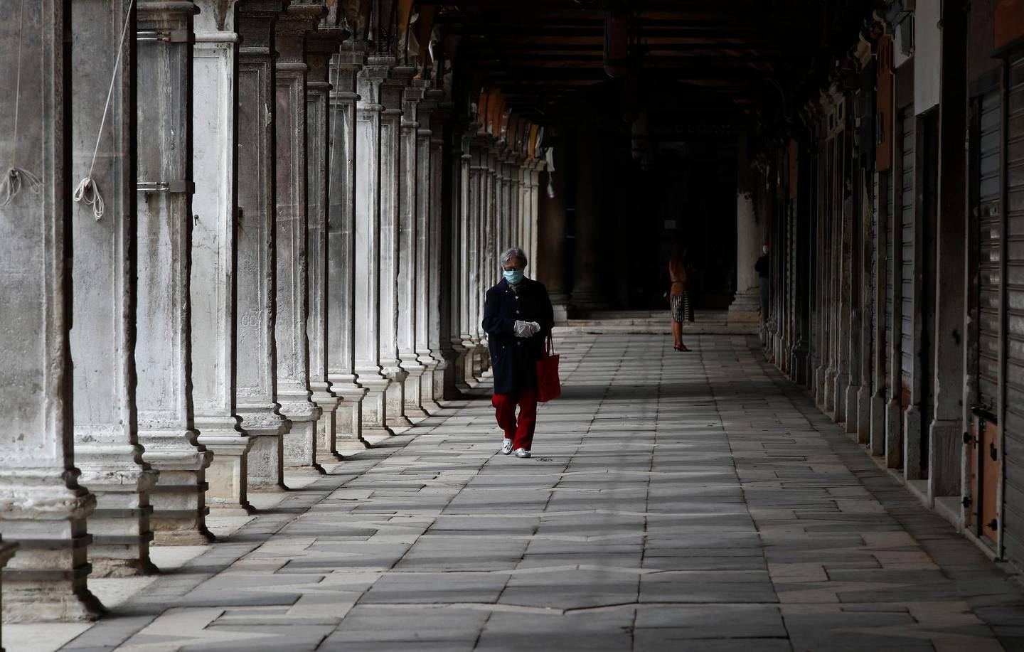 In this picture taken on Wednesday, May 13, 2020, a woman wearing a sanitary mask walks at St. Mark's Square in Venice, Italy. Venetians are rethinking their city in the quiet brought by the coronavirus pandemic. For years, the unbridled success of Venice's tourism industry threatened to ruin the things that made it an attractive destination to begin with. Now the pandemic has ground to a halt Italyâ€™s most-visited city, stopped the flow of 3 billion euros in annual tourism-related revenue and devastated the city's economy. (AP Photo/Antonio Calanni)