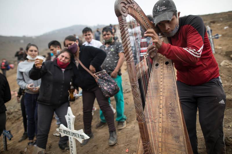 Harpist and cemetery worker Charlie Juarez performs while Gregoria Zumaeta, 44, left, mourns the death of her brothers Jorge Zumaeta, 50, and Miguel Zumaeta, 54, who died from Covid-19, at the Nueva Esperanza cemetery on the outskirts of Lima, Peru. AP Photo