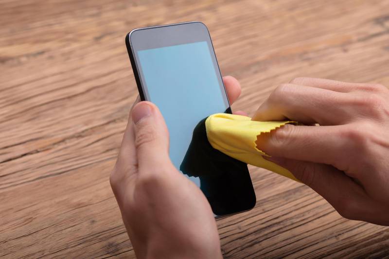 R3EJ77 Man Cleaning Mobile Phone Screen With Yellow Cloth Over Wooden Desk. Alamy