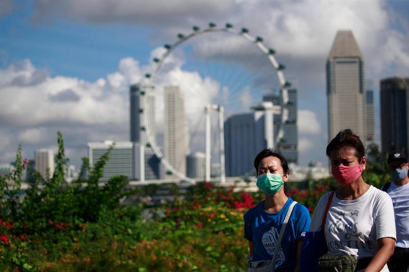 People wearing masks walk with the Singapore Flyer and The Central Business district area in the background in Singapore. EPA