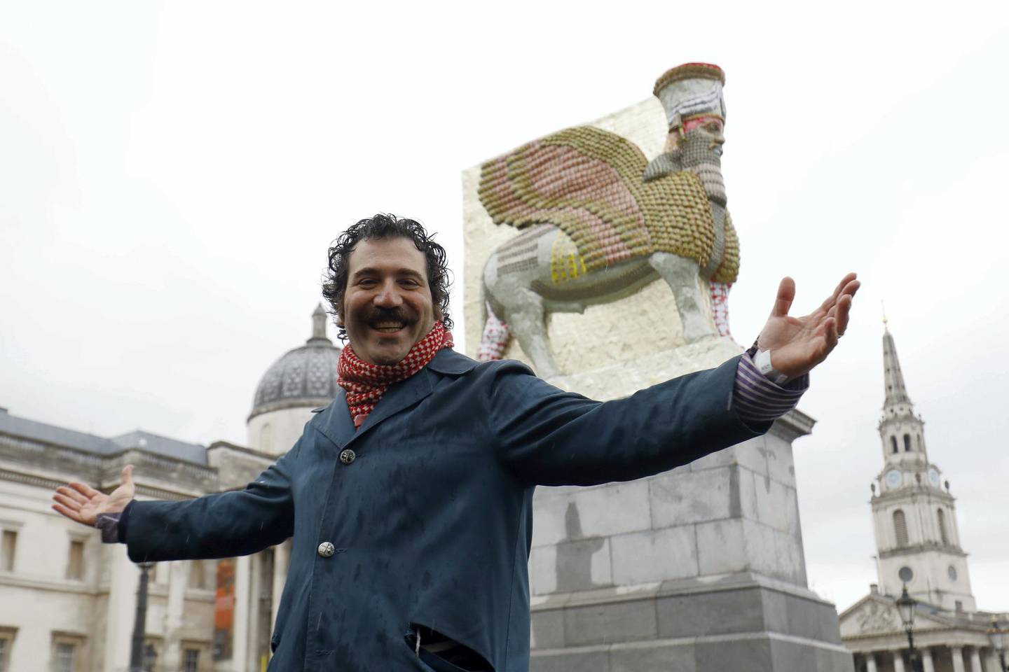 Iraqi-American artist Michael Rakowitz poses in front of his sculpture "The Invisible Enemy Should Not Exist" standing on the Fourth Plinth in Trafalgar Square in London on March 28, 2018 after it was unveiled. - The sculpture, made from 10,500 empty date syrup cans, is a recreation of a first-millenium-BC Lamassu, a winged bull and protective deity, that stood at the entrance to Nergal Gate of Nineveh and was destoryed by the Islamic State group in 2015. (Photo by Tolga AKMEN / AFP) / RESTRICTED TO EDITORIAL USE - MANDATORY MENTION OF THE ARTIST UPON PUBLICATION - TO ILLUSTRATE THE EVENT AS SPECIFIED IN THE CAPTION