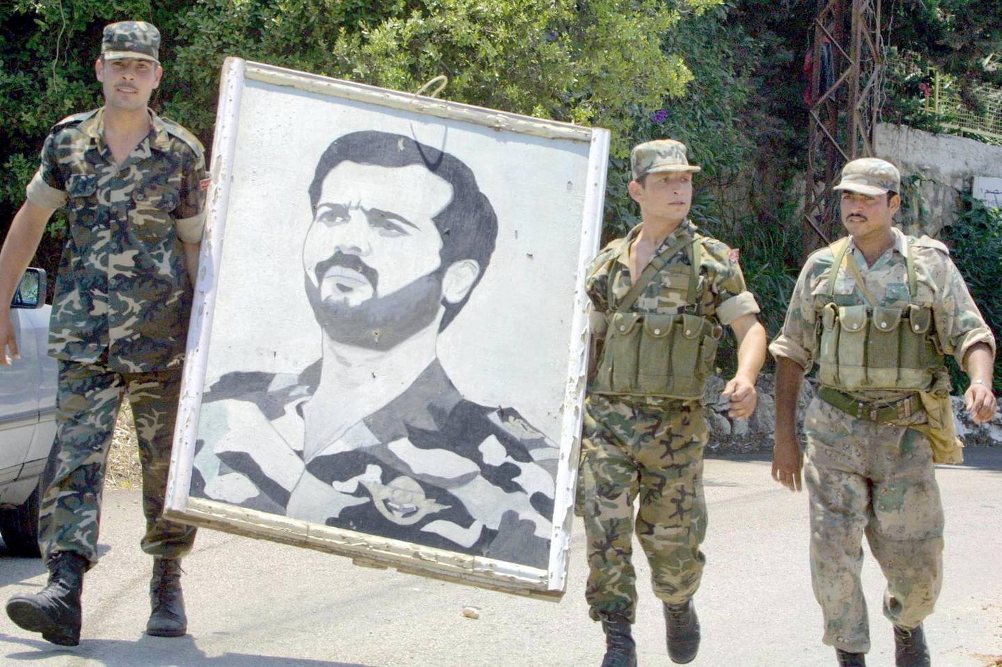 Syrian soldiers carry a portrait of Syrian president Bashar al-Assad's late brother, Bassel, as they dismantle one of their posts in Yarze on the Beirut-Damascus highway 14 June 2001. Syrian troops based in Beirut and areas close to the Lebanese capital began yesterday redeploying their forces in an operation scheduled to last several days. AFP PHOTO/Ramzi HAIDAR (Photo by RAMZI HAIDAR / AFP)
